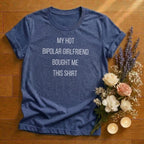 Blue heather t-shirt with text 'My hot bipolar girlfriend bought me this shirt' on a wooden surface with flowers and candles.