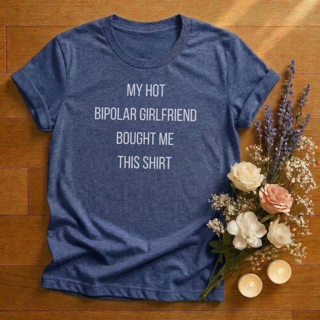 Blue heather t-shirt with text 'My hot bipolar girlfriend bought me this shirt' on a wooden surface with flowers and candles.