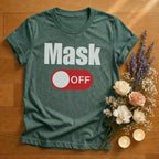 Green heather t-shirt with 'Mask Off' graphic on a wooden surface with flowers and candles.